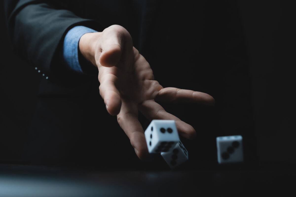 サイコロを投げるビジネスマンの手元。リスクや運を象徴する瞬間